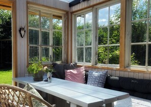 Ein Wintergarten mit großen Fenstern, einem weißen Tisch und einer schwarzen Couch.