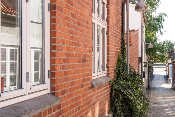 A narrow brick building with large windows and a narrow sidewalk.