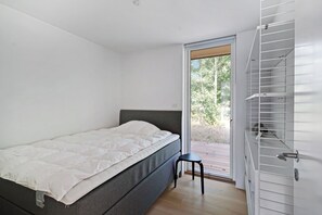A modern bedroom with a bed, a small stool, and a sliding door leading to an outdoor area.