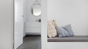 A modern bathroom with a white vanity, a round mirror, and a bench with pillows. - Holiday home on Bornholm close to sea and beach (Aakirkeby)