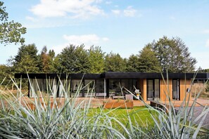 Een modern huis met grote glasramen, een houten terras en een gazon.