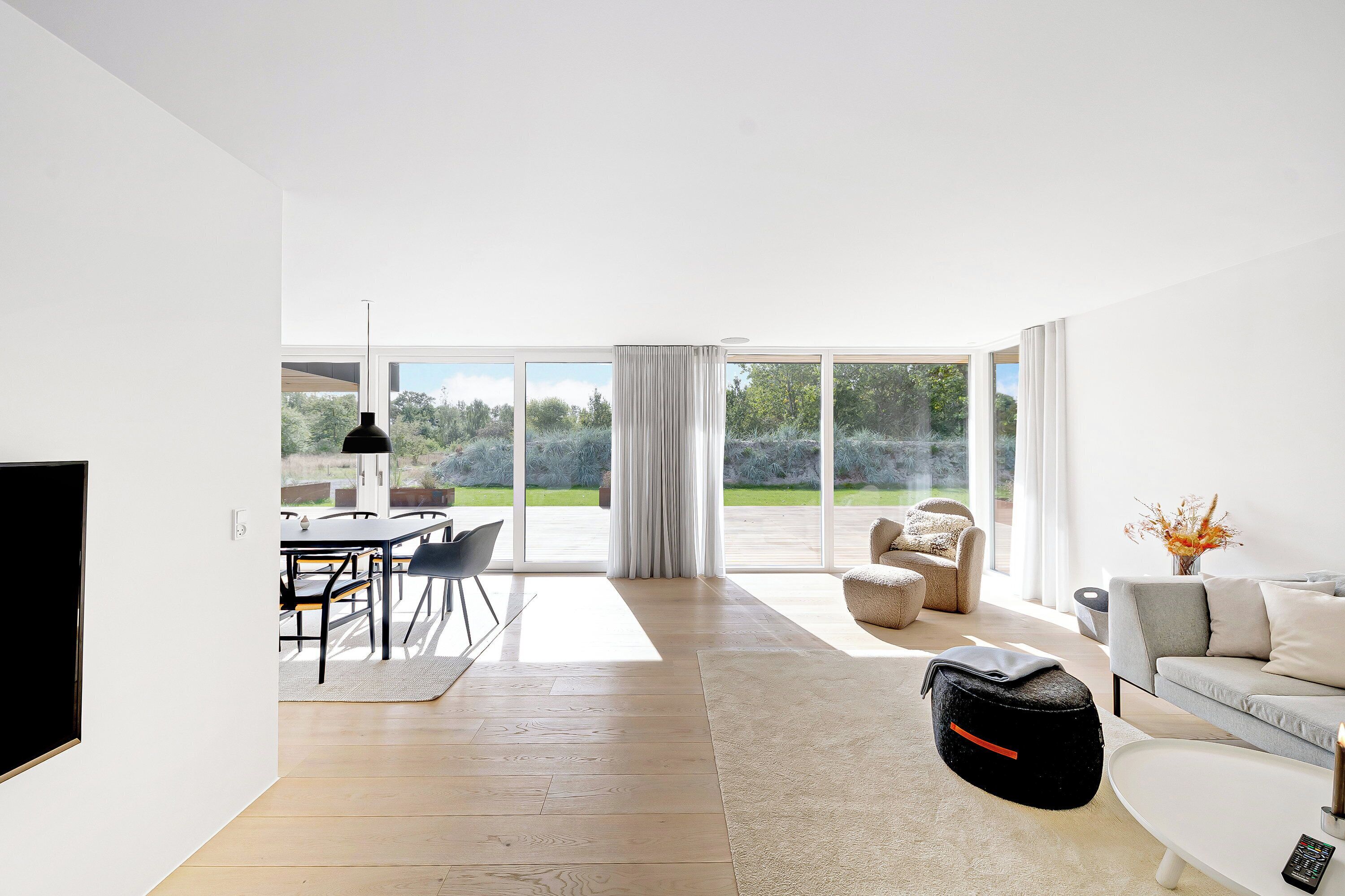 A spacious living room with a large window, a sofa, a coffee table, and a dining area with chairs and a table.
