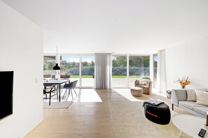 Un salon spacieux doté d’une grande fenêtre, d’un canapé, d’une table basse et d’un coin repas avec des chaises et une table.