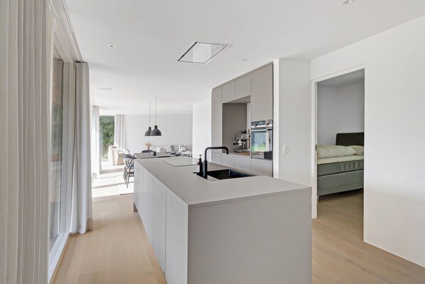 A modern kitchen with a central island, a dining area with a table and chairs, and a bedroom with a bed and nightstand.