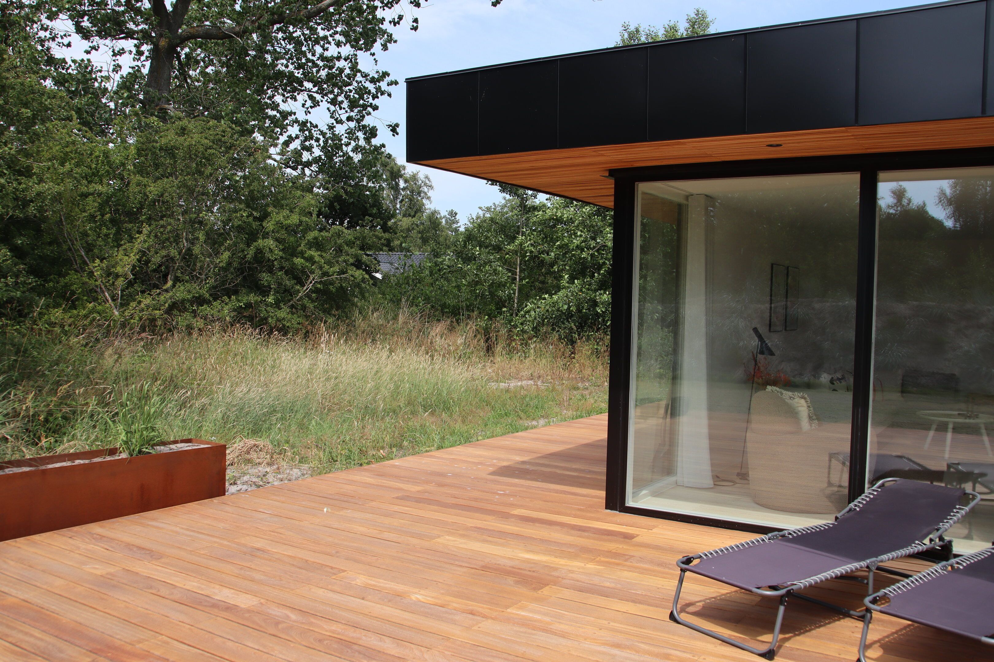 A modern outdoor deck with wooden flooring and two lounge chairs.