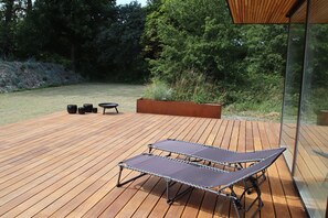A wooden deck with two lounge chairs, a small table, and a planter.