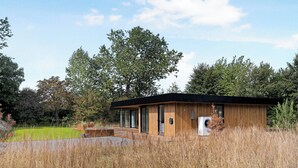 A modern wooden cabin with large windows, a deck, and a grassy field in the background. - Holiday home on Bornholm close to sea and beach (Aakirkeby)