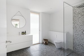 Une salle de bain moderne avec un grand miroir rond, un meuble-lavabo blanc et une cabine de douche en verre.