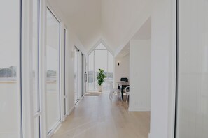 Un intérieur moderne avec un long couloir menant à une salle à manger, de grandes fenêtres et une plante en pot.