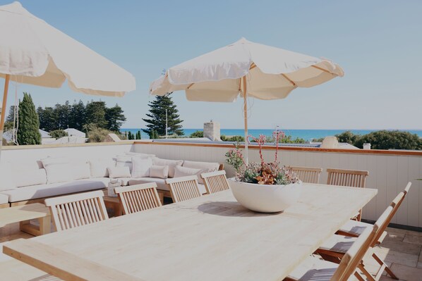 Une terrasse sur le toit, avec une table et des chaises, un canapé et deux grands parasols.