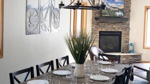 A dining area with a stone fireplace, a mounted TV, and a dining table set for six.