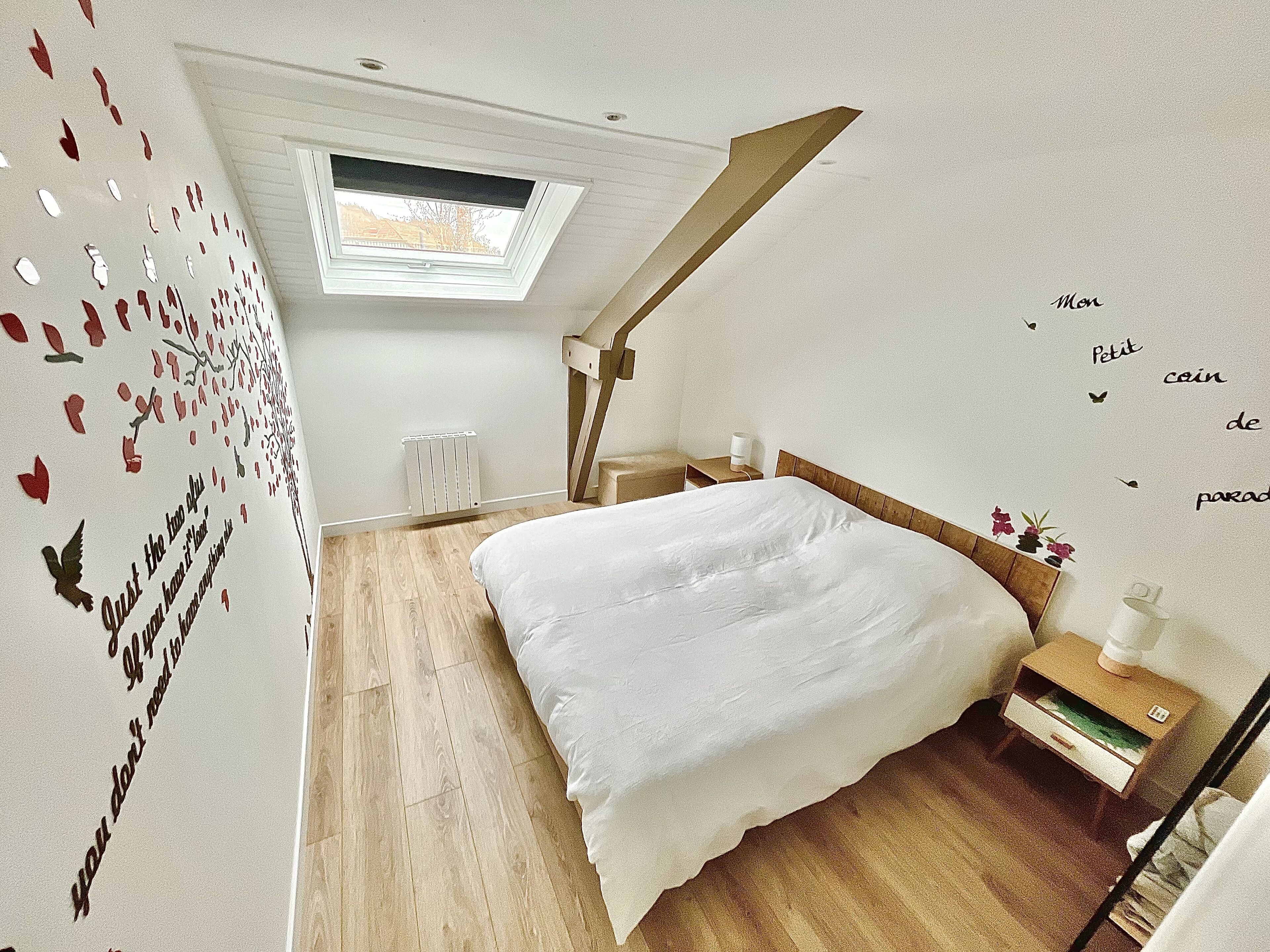 Une chambre avec un puits de lumière, un lit, une table de chevet et un mur agrémenté d’éléments décoratifs.