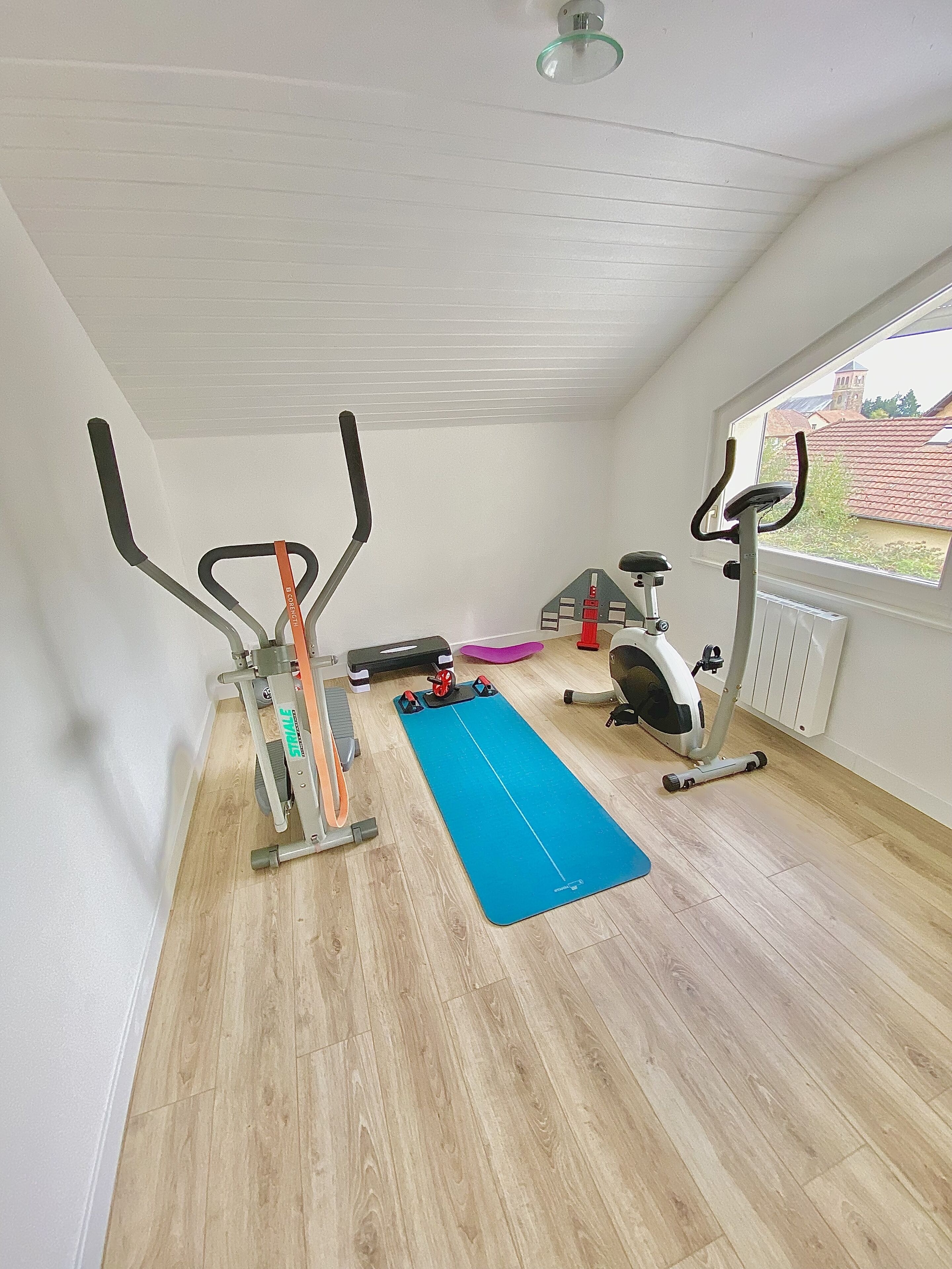 Un gimnasio en casa con dos bicicletas estáticas, una colchoneta azul y una bicicleta fija.