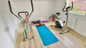 Un gimnasio en casa con dos bicicletas estáticas, una colchoneta azul y una bicicleta fija.