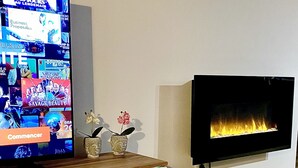 Ein Wohnzimmer mit einem Flachbildfernseher, der einen Film zeigt, zwei Sektgläser auf einem Tisch und einem Kamin.