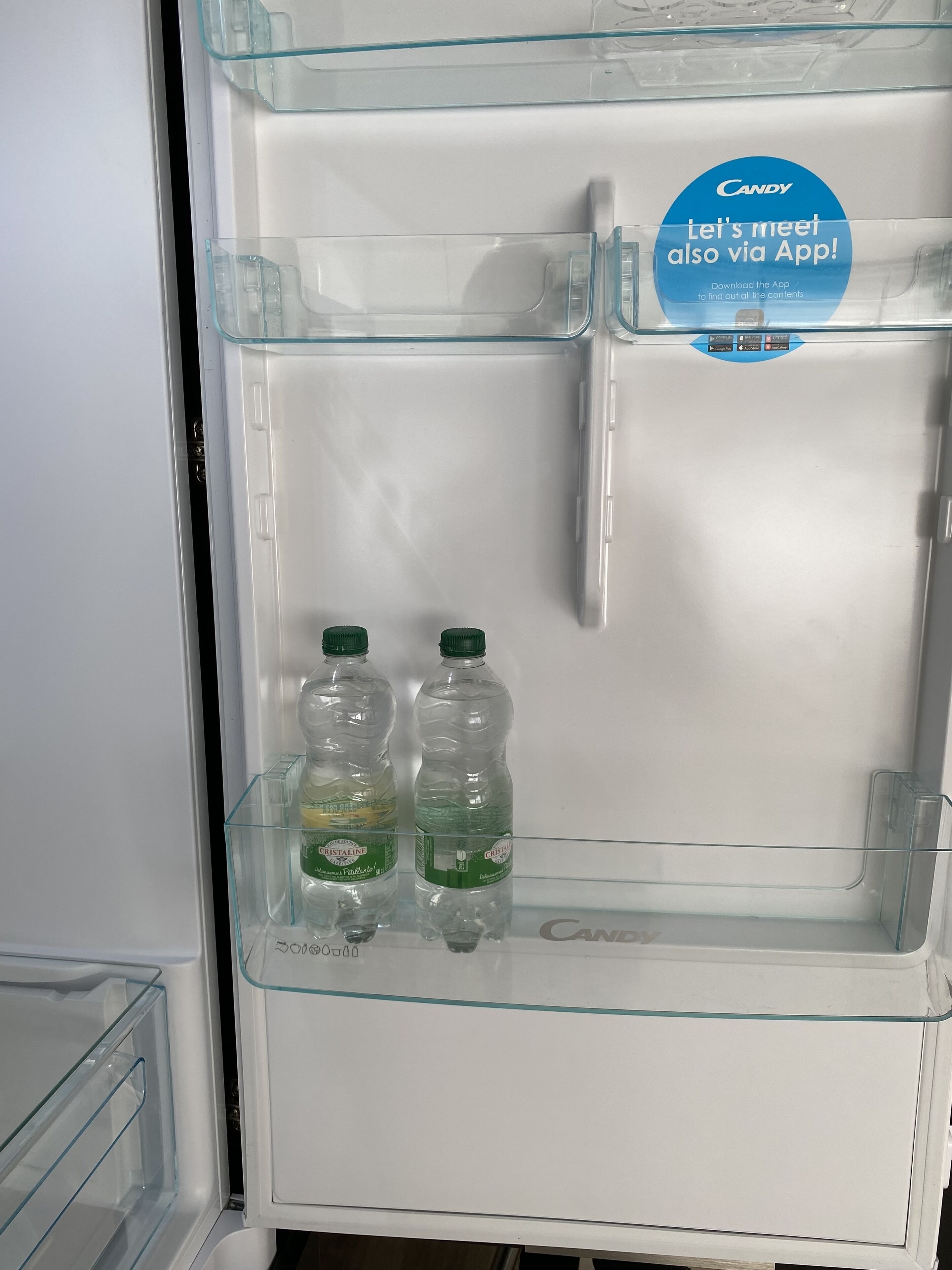An open refrigerator with two bottles of Cristaline water on the door shelf.