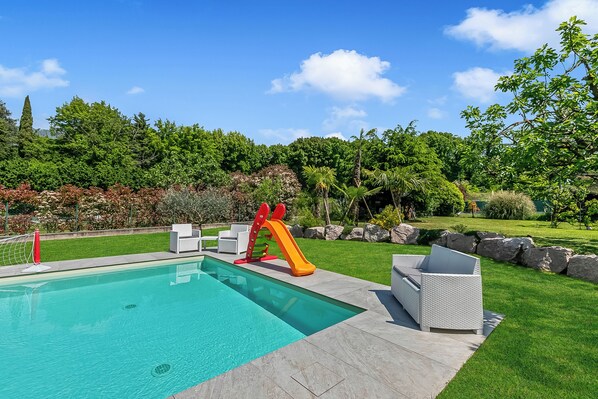 Une piscine avec un toboggan, entourée d’une pelouse bien entretenue et d’arbres.