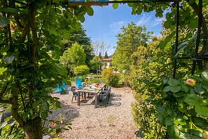 Un espace extérieur aménagé pour les repas, avec une table et des chaises, entouré de verdure et avec une maison en arrière-plan.