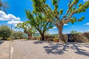 Un patio lastricato di ghiaia con un albero grande, sedute all'aperto e un muro in pietra.