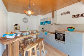 A modern kitchen with wooden stools, a dining table, a clock, and a sign that says 'ENTRANCE HOME IS WHERE YOUR STORY BEGINS.'