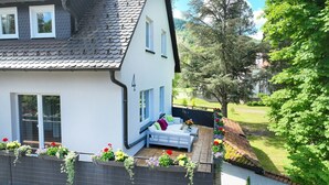 Ein Haus mit weißer Fassade, einem grauen Dach und einem Balkon mit einer blauen Bank und Blumenkästen.