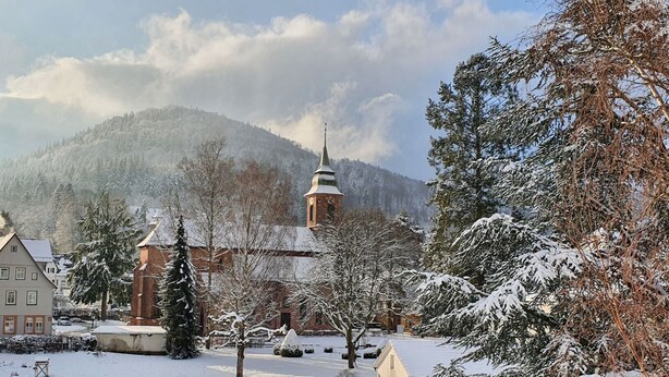 Ein schneebedecktes Dorf mit Kirche, Häusern und Bäumen.