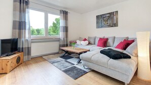 Ein modernes Wohnzimmer mit einer Couch, einem Couchtisch, einem Fernseher und einem Fenster mit Vorhängen.