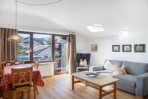 Una sala de estar con un sofá, una mesa, una silla y una ventana que ofrece vistas a casas y montañas.
