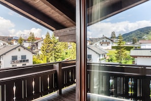 Un balcone con ringhiera in legno, vista su case e una montagna sullo sfondo.