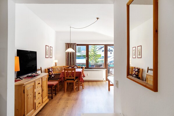 Una habitación con televisión, muebles de madera, una mesa de comedor y un ventanal con vistas.