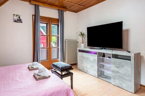 Une chambre à coucher avec un lit, un téléviseur posé sur un meuble, un radiateur et une fenêtre avec des rideaux.