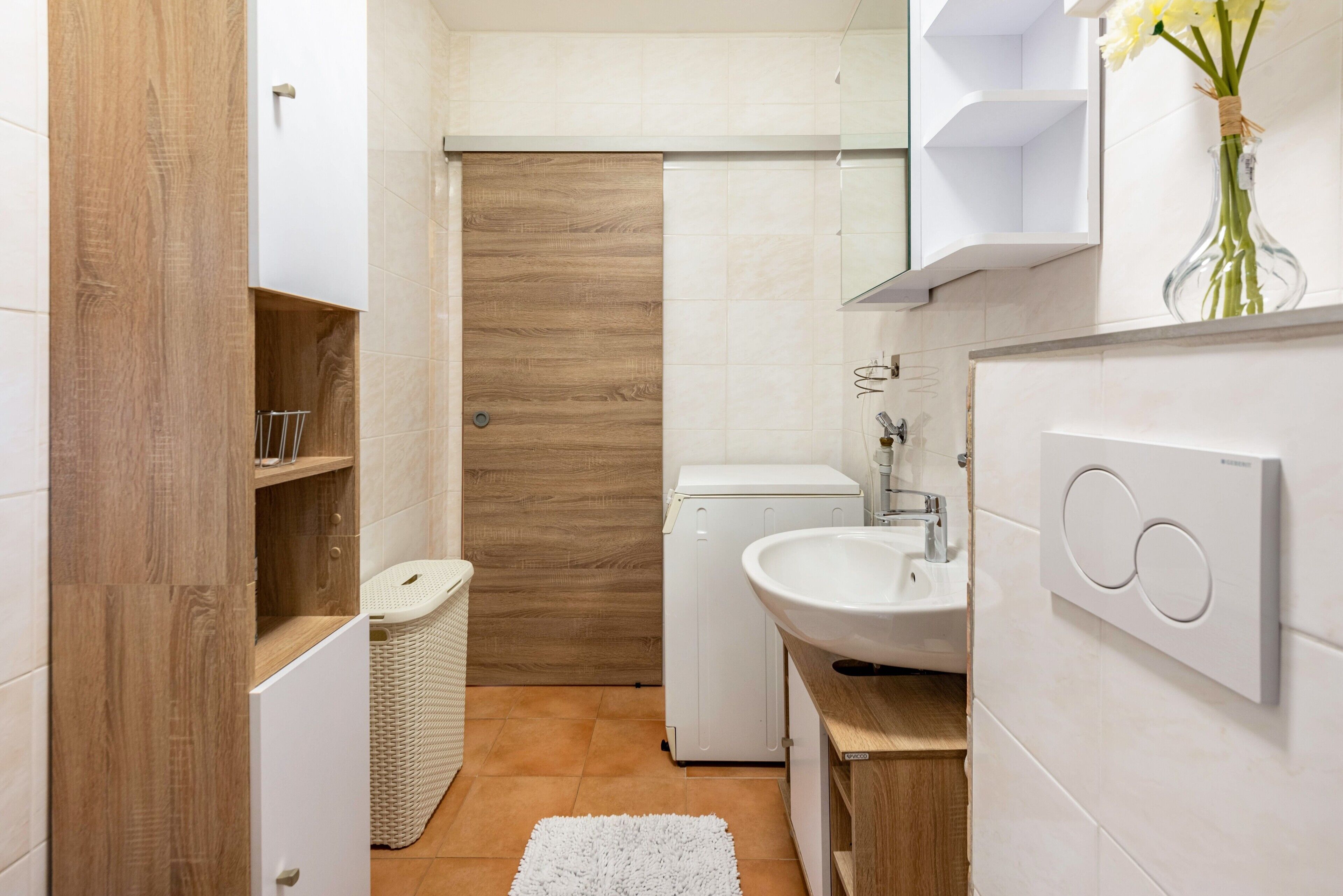 A modern bathroom with a wooden vanity, a white sink, and a shower.