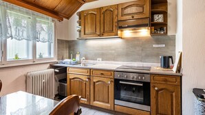 Una cocina con armarios de madera, un horno de acero inoxidable, un lavamanos y una ventana con cortinas de encaje.