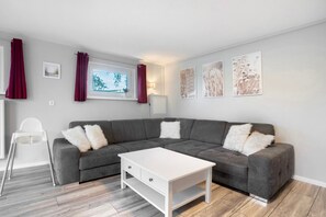 A modern living room with a grey sectional sofa, white coffee table, and a window with curtains.