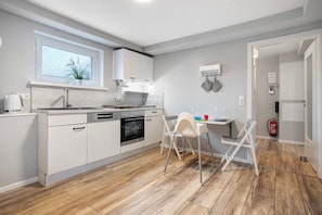A modern kitchen with white cabinets, a built-in oven, and a dining area with a white table and chairs.