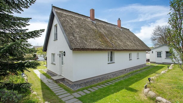 Een wit huis met rieten dak, een pad van stenen en een kleine tuin.