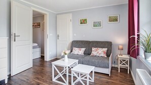 Een kamer met een grijze bank, witte meubels, een bijzettafeltje en een plant in pot.