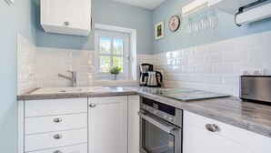 Een moderne keuken met witte kasten, een ingebouwde oven, een koffiezetapparaat en een raam.