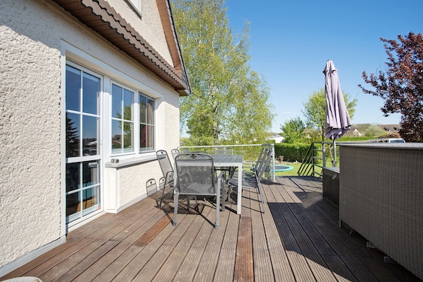 Una terraza con mesa y sillas, un espacio exterior cubierto y una casa con ventana.