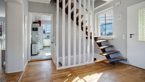 Un escalier avec des marches en bois et une rampe blanche, menant à une pièce dotée d’une fenêtre et d’une porte.