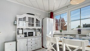 Une cuisine avec des meubles blancs, un four à micro-ondes, un réfrigérateur et une table à manger avec des chaises.