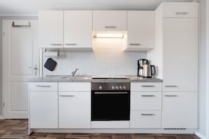Une cuisine moderne avec des meubles blancs, un four encastré, une machine à café et un pare-feu en carreaux.