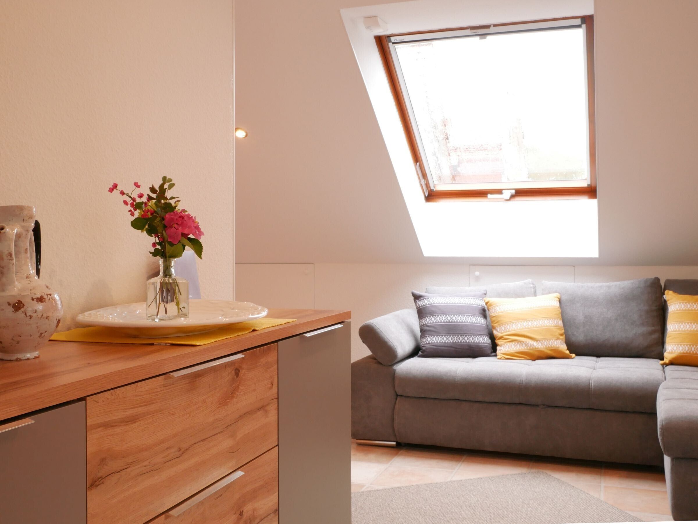 A modern living room with a grey sofa, a wooden sideboard, and a skylight above.