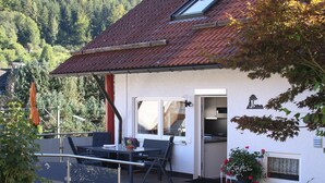 A house with a red-tiled roof, a balcony with a table and chairs, and a view of a forested hillside. - Holiday Apartment "Am Eiberg" with Mountain View, Private Terrace & Wi-Fi (Bad Wildbad)