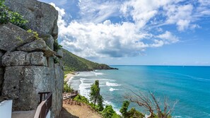 A coastal view with a rocky cliff, a wooden deck, and a beach. - Mini Cooper - The Cooper Bay Villas Tortola BVI (Tortola)