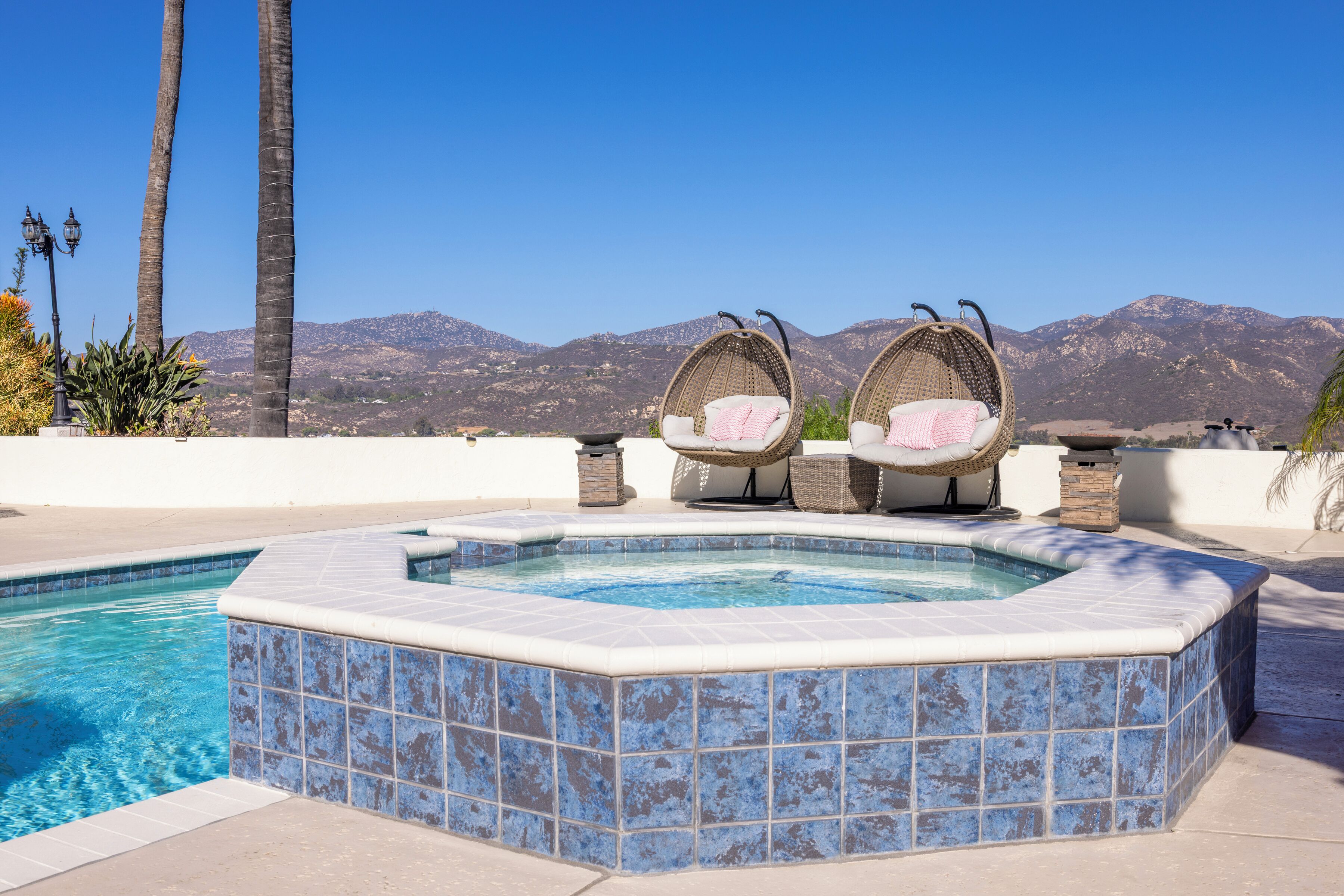Un jacuzzi con dos sillas de mimbre, una piscina y montañas al fondo.