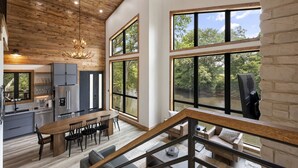 A modern kitchen with a dining area, large windows, and a staircase leading to a loft bedroom.