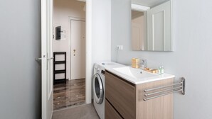Un baño moderno con lavadora, un lavabo con espejo y un perchero para toallas.