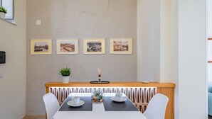Un comedor con una mesa blanca, cuatro sillas, una pequeña planta en maceta y cuatro cuadros en la pared.