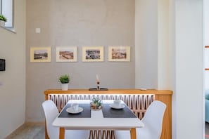 A dining area with a white table, four chairs, a small potted plant, and four framed pictures on the wall.